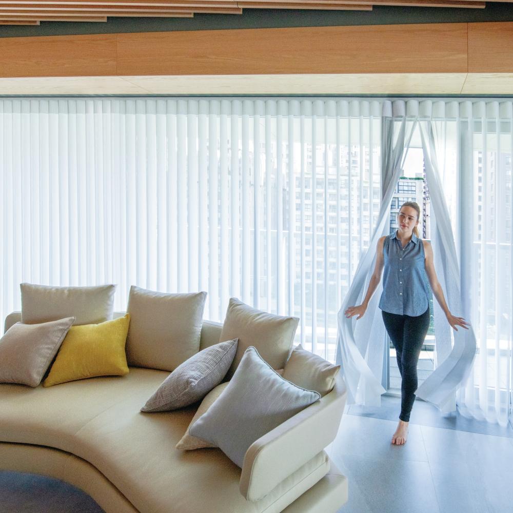 Balkon kapısında dikey tül perde dilimlerinin arasından geçen kadın